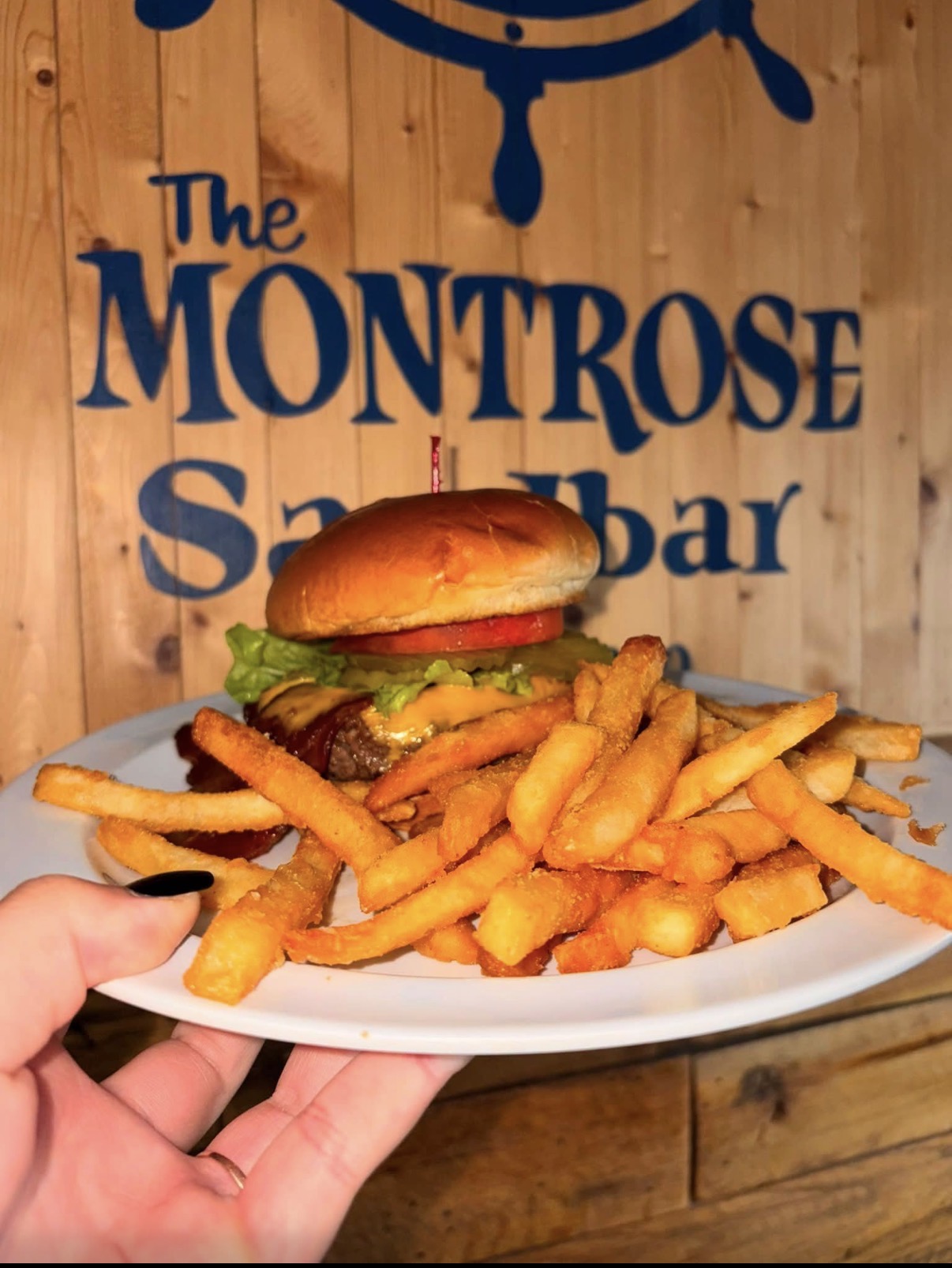 Burger and fries plate in front of The Montrose Sandbar sign